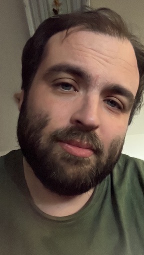 Portrait photograph of Joshuah Rainstar with a full brown beard, blue-gray eyes, and an olive shirt